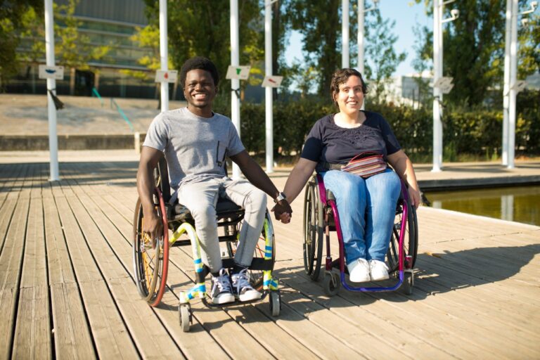 Loving man and woman in wheelchairs spending time near water. African American man and Caucasian woman in casual clothes, holding hands. Love, affection, happiness concept